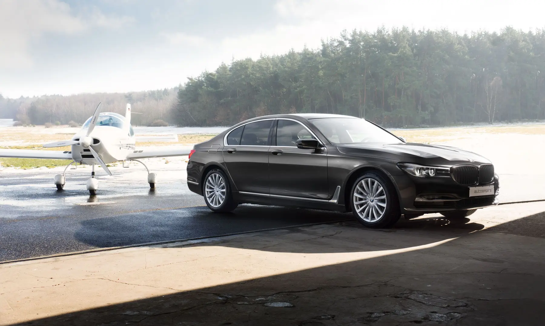 Executive BMW 7 Series sedan beside a private aircraft at an airport