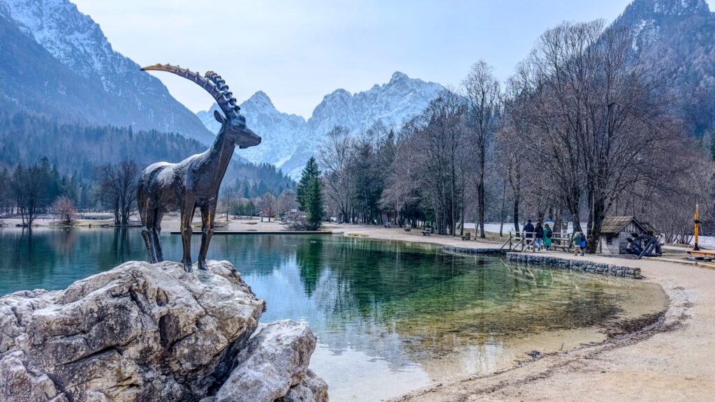 Alpine lake and ibex sculpture beneath snow-covered mountains in Slovenia