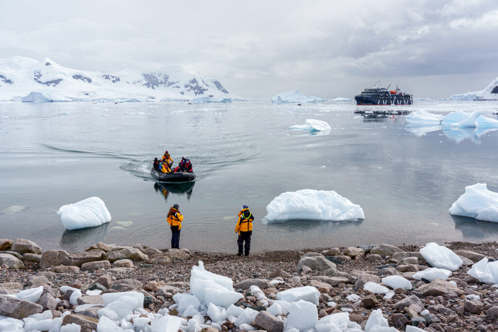 An expedition ship, Zodiac and landing team in an Antarctic bay