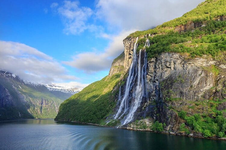 A Norwegian fjord framed by steep green mountains and a waterfall