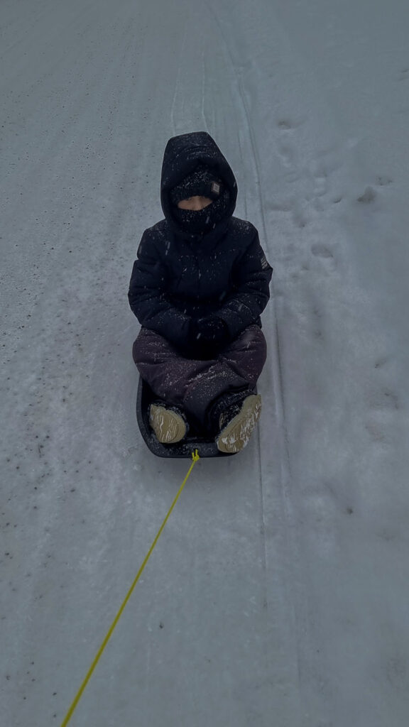 Child riding a sled during snowfall in Vuokatti