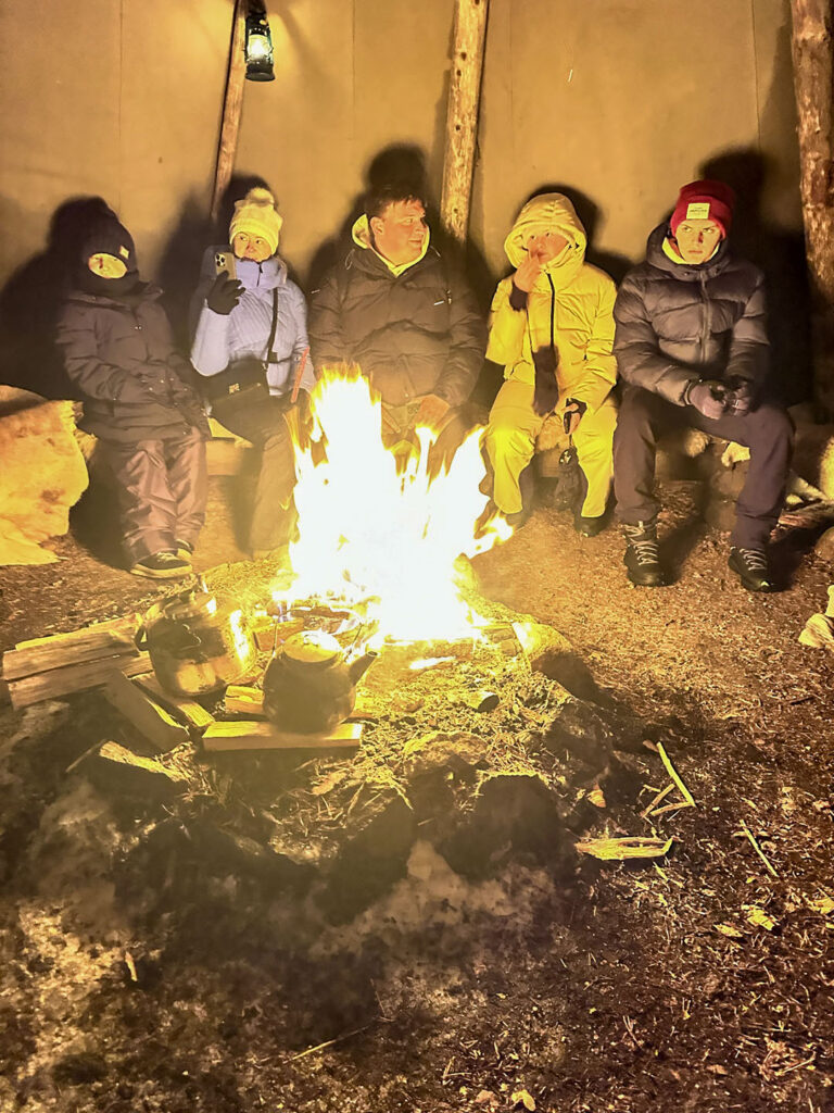 Family gathered beside an outdoor fire in the snowy forest near Vuokatti
