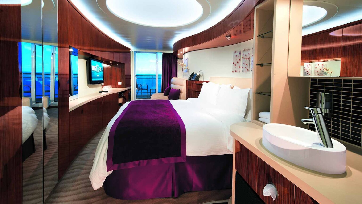 Bed, seating area and balcony access in a Club Balcony Suite on Norwegian Epic