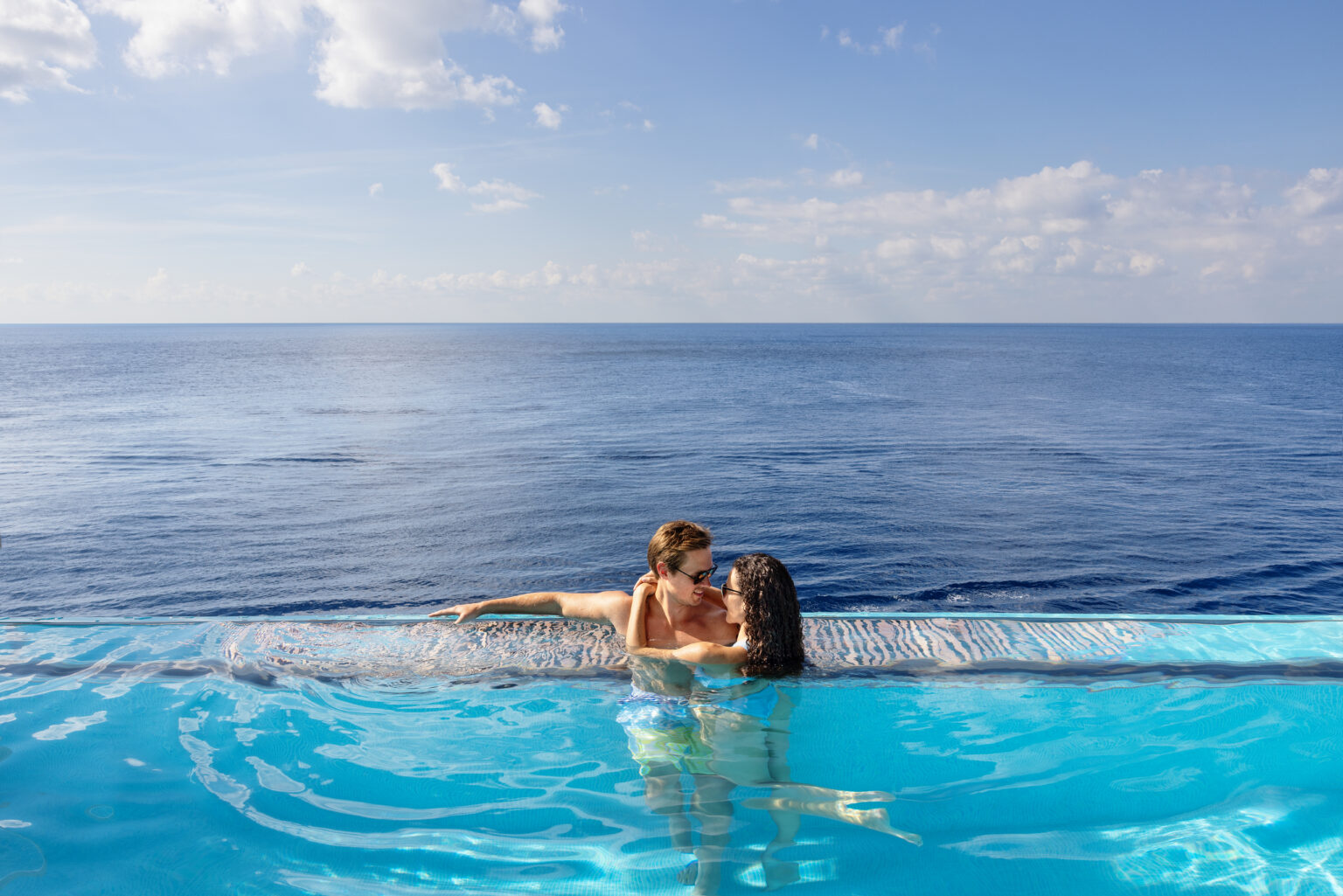 A couple relaxing in the Infinity Beach pool on Norwegian Prima with a sea view